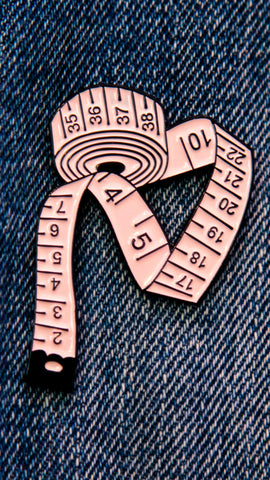 Pin's représentant un mètre ruban de couture, couleur rose.